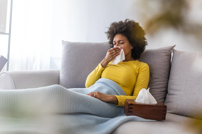 A woman sitting on a couch blowing her nose.