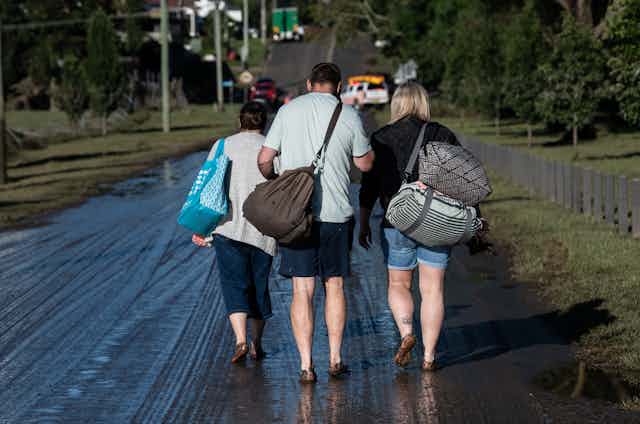 Three flood victims carrying bags with backs to camera