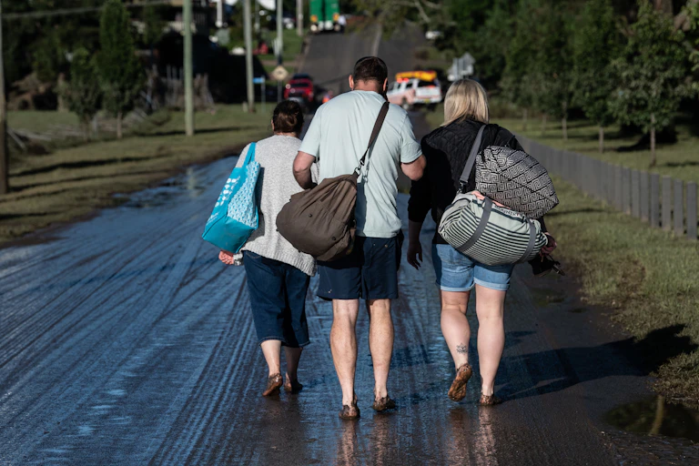 Three flood victims carrying bags with backs to camera