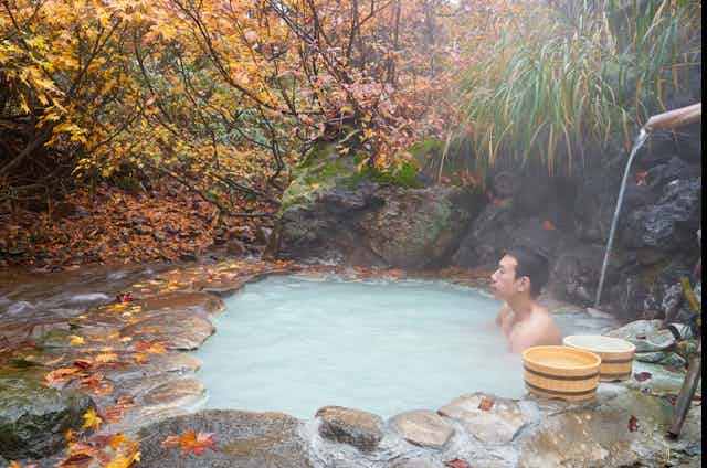 Un homme est assis dans une piscine d’eau chaude laiteuse sous un feuillage d’automne.