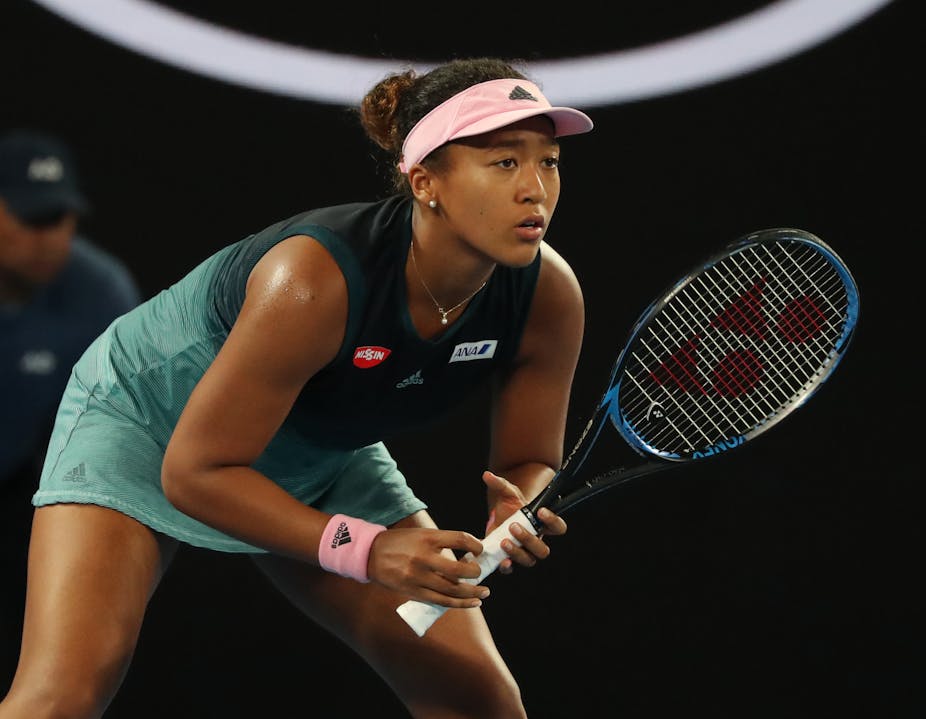 Naomi Osaka in the middle of a tennis match, prepared to hit the ball.