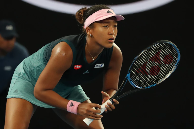 Naomi Osaka in the middle of a tennis match, prepared to hit the ball.