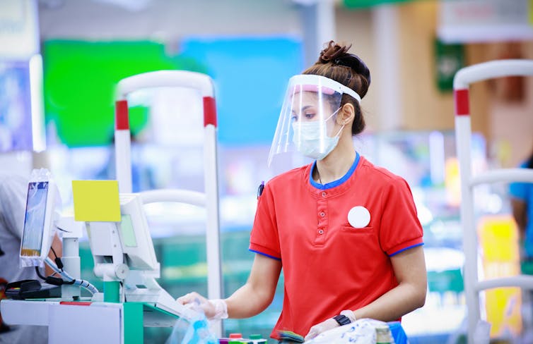 A female grocery store cashier wearing a face mask and shield.