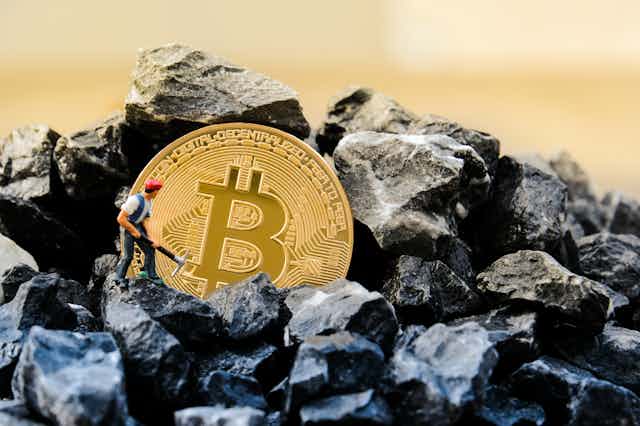 A figurine mines coal with a giant bitcoin in the middle.