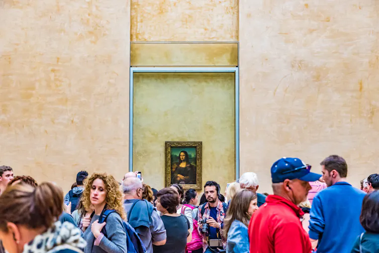 Crowd of tourists in front of Mona Lisa on gallery wall.