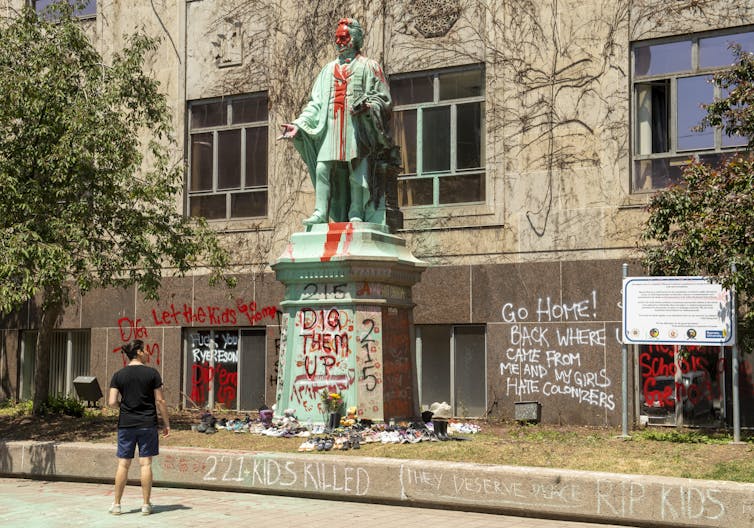 A woman looks at a spraypainted statue of Egerton Ryerson.