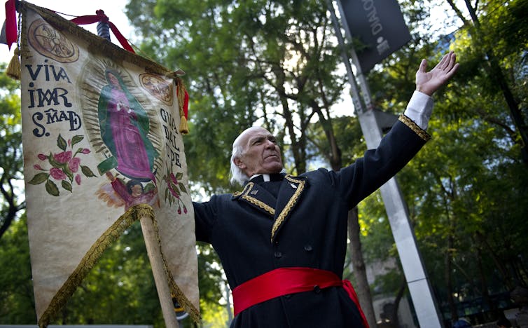 A man dressed as Miguel Hidalgo performs with an image of the Virgin of Guadalupe at the beginning of the 'Relief for Peace with Justice and Dignity' caravan in Mexico City on June 4, 2011.