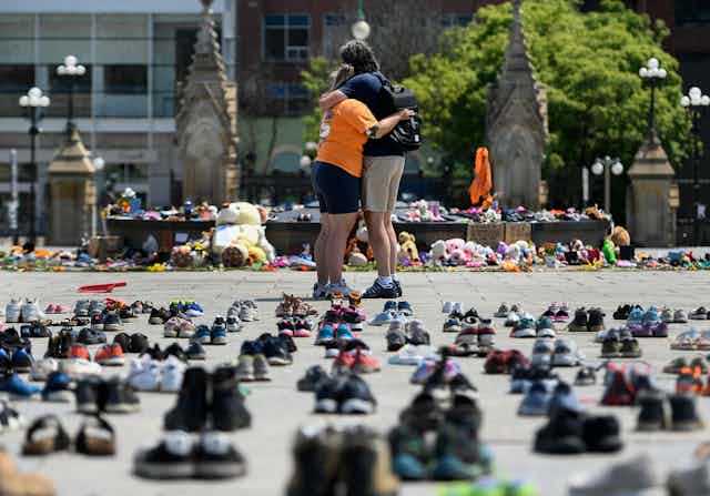 People hug in front of 215 shoes to represent the Indigenous children's remains that were found