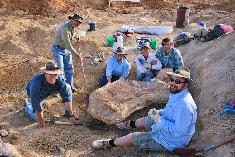 Scientists in hats sitting around a refrigerator-sized bone fragment.