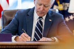 Joe Biden signs a bill at his desk in the Oval Office.