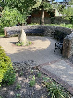 Black benches arranged against a low, semi-circular stone wall in a Chichester park