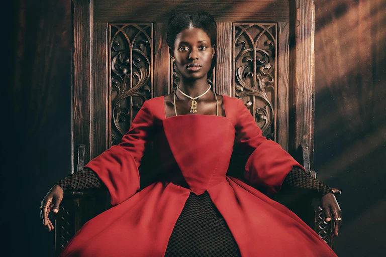Woman in period dress sits in thrown.