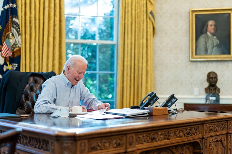 Joe Biden sitting in the Oval Office making a call to Boris Johnson in the UK.