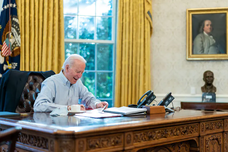 Joe Biden sitting in the Oval Office making a call to Boris Johnson in the UK.