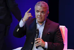 A man gestures while speaking into a microphone.