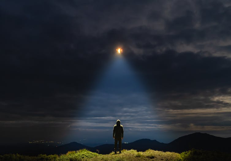 Artist's concept of a UFO shining on a male standing on the mountain