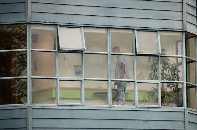 A worker is seen through a window cleaning surfaces. 