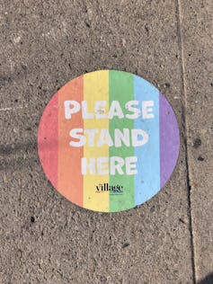 'Please stand here' social distancing sticker in Pride colors