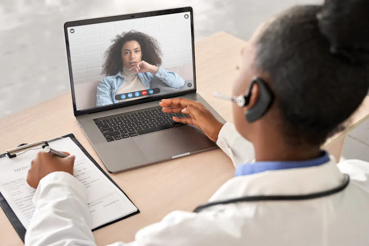 A doctor wearing a headset consults a female patient during a video call on laptop screen