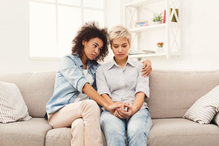 Female friends sit on a couch, supporting each other.