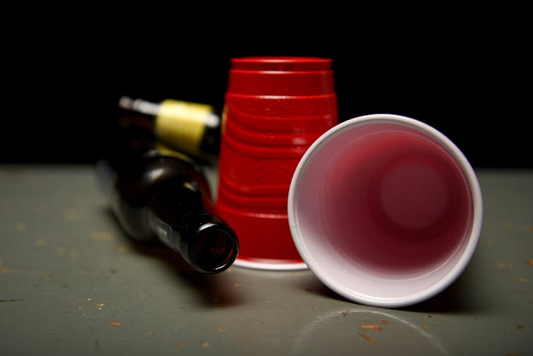 Two empty red plastic cups next to tipped over beer bottles.