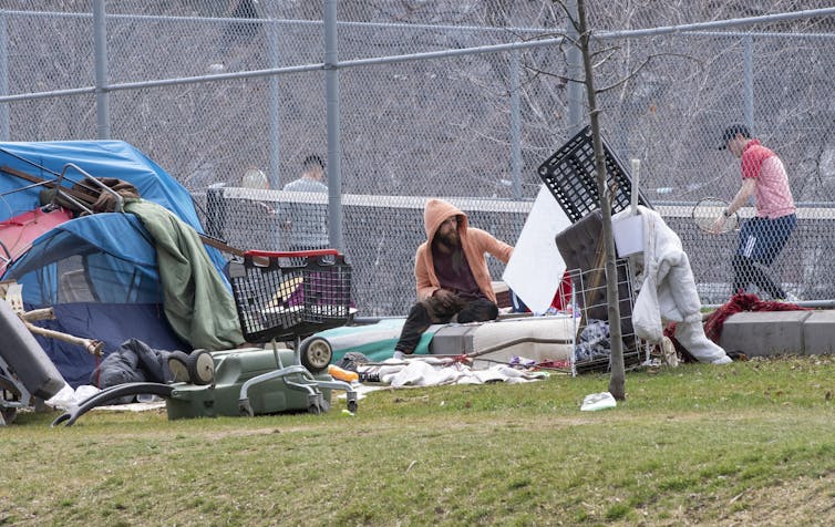 A man sitting in front of a tennis court, next to a tent and shopping carts.