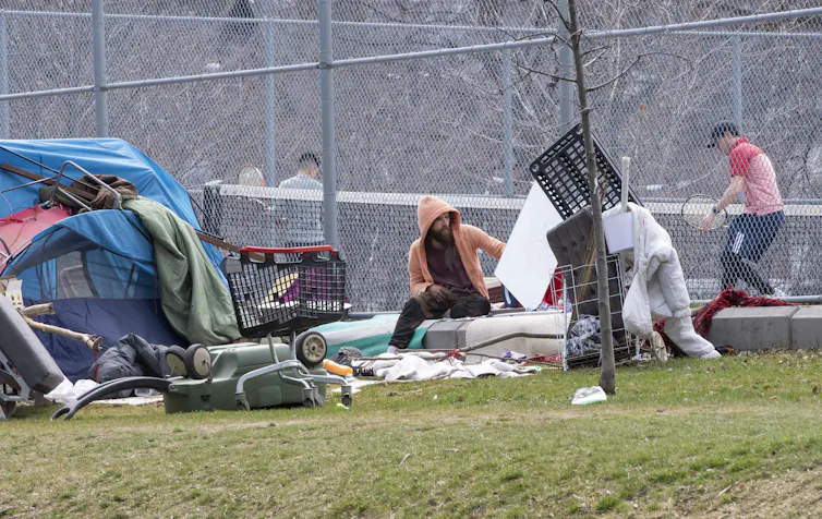 A man sitting in front of a tennis court, next to a tent and shopping carts.