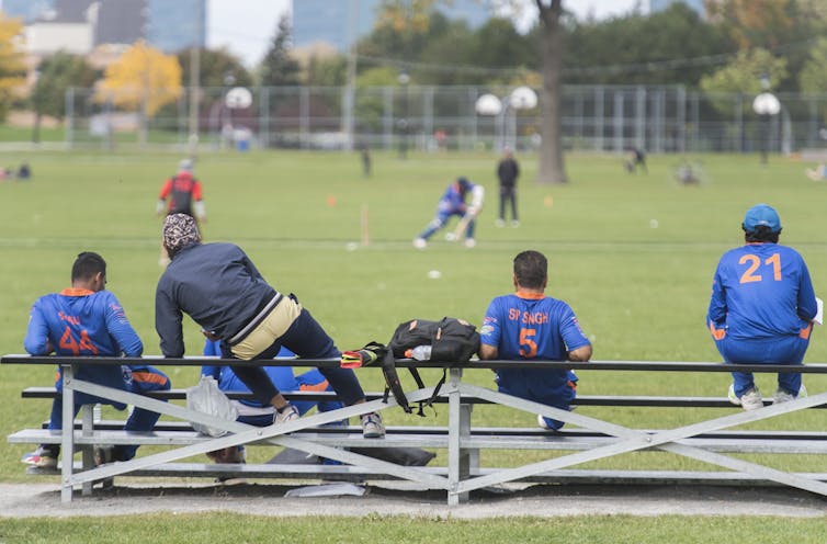 Men sitting on bleachers watching a cricket game