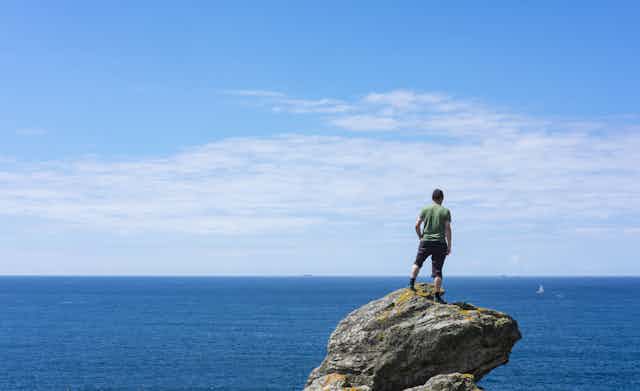 Seorang pria berdiri di atas bebatuan di lautan. 