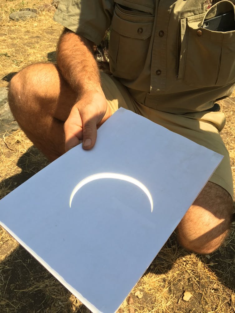 Someone holding a piece of paper with a crescent shape patch of light projected onto it.