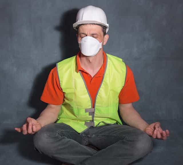 A man in a high-visibility vest and hard hat sitting in a meditative pose