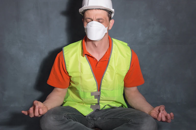 A man in a high-visibility vest and hard hat sitting in a meditative pose