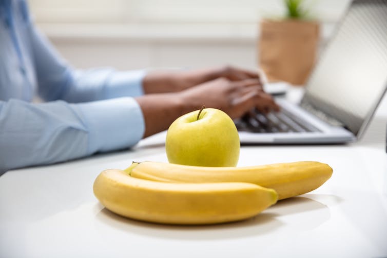 A close-up of an apple and two bananas on an office desk.
