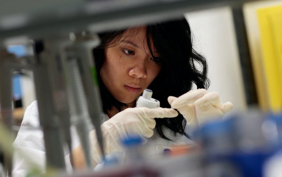 A woman wearing a white coat and gloves in a lab.
