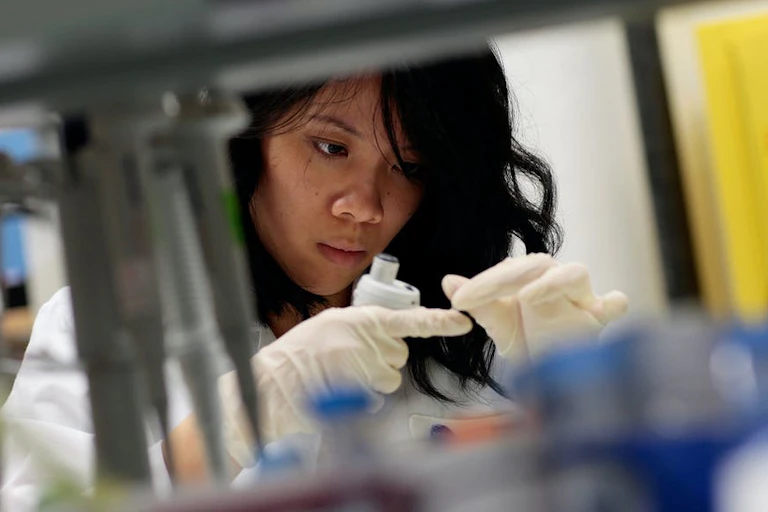 A woman wearing a white coat and gloves in a lab.