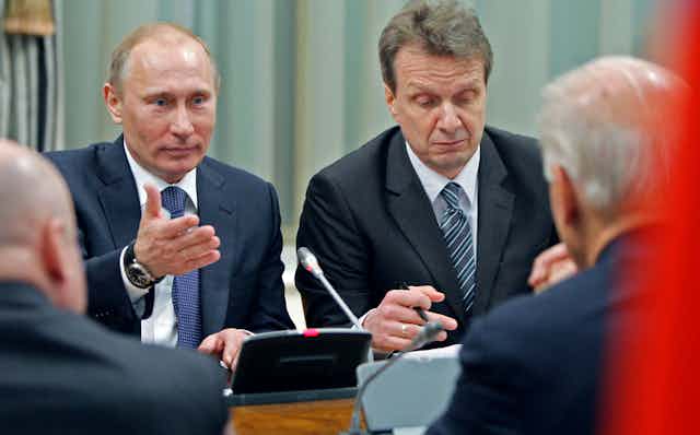 Vladimir Putin gestures with his hand at Joe Biden, whose back is turned, while sitting at a table in Moscow in 2011