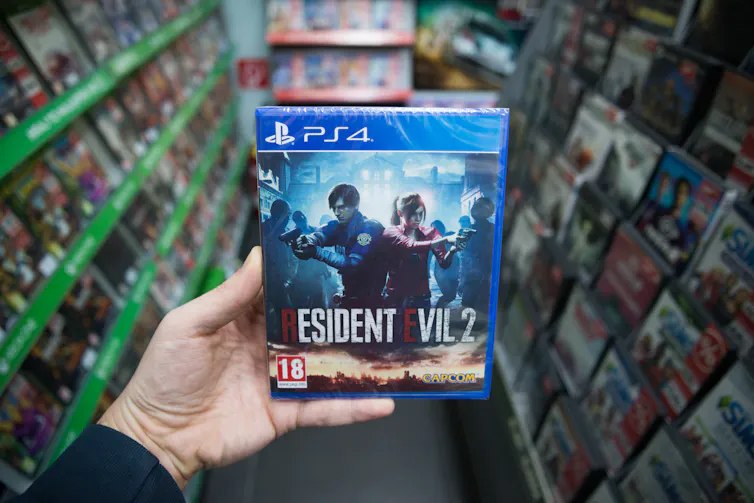 A person's hand holding the game 'Resident Evil 2.'