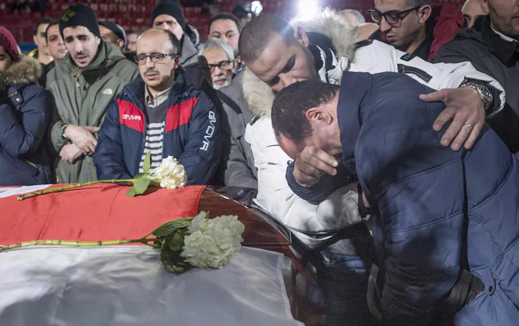 Mourners at a funeral are in tears and console each other as they lean over caskets