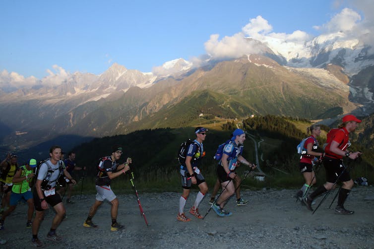 Several competitors run with walking poles up a hill in the French Alps