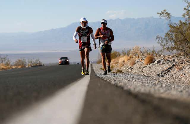 Two ultra-marathoners struggle in the heat on a road in the desert