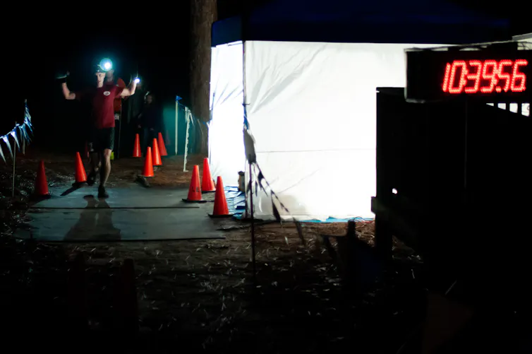 The winner of an ultramarathon in North Carolina raises his hands as he crosses the finish line at night
