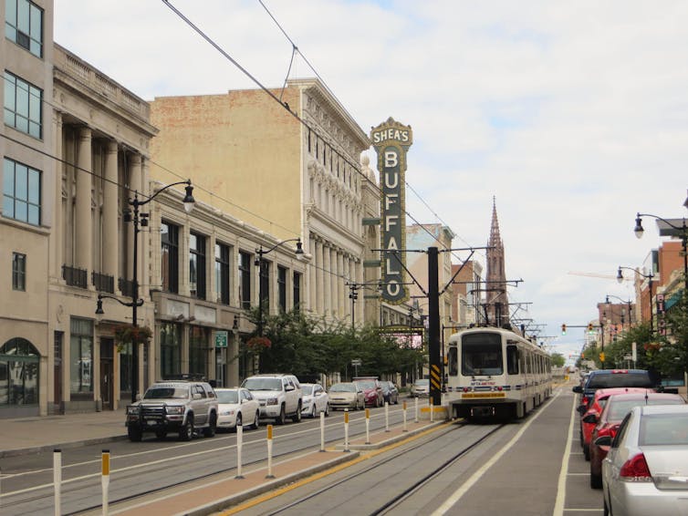 A city street with cars parked on the sides, lined with a theater and other buildings.