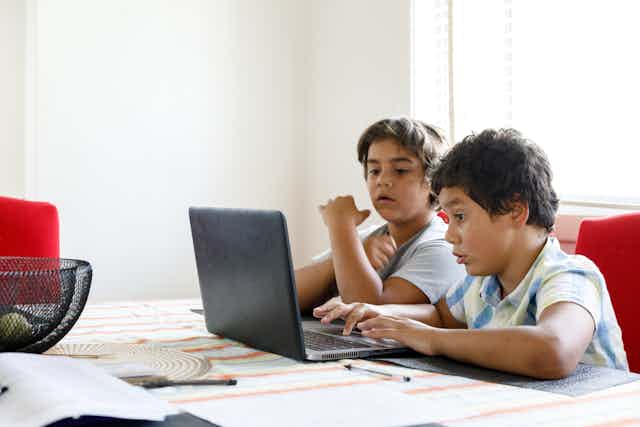 Two children are sitting at a laptop