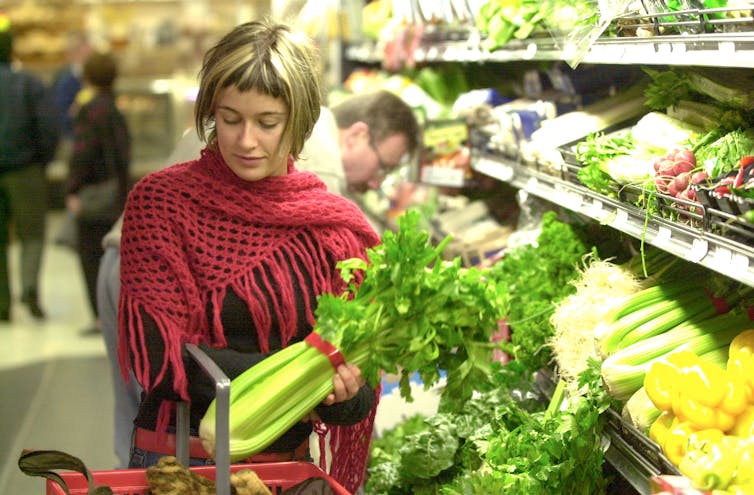 A shopper selects celery at a supermarket.