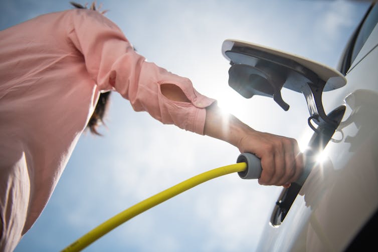 woman's arm holds EV charger on car