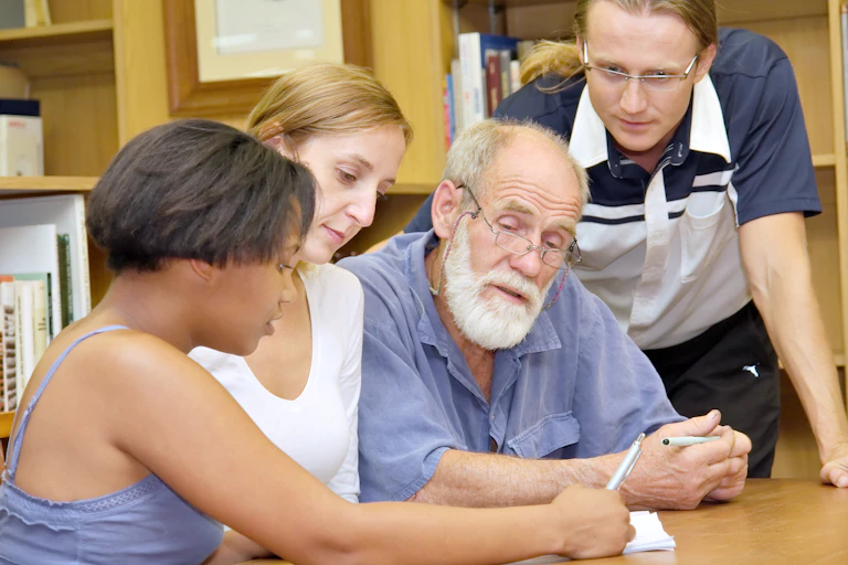 Three young students and an older student work on a problem in the library
