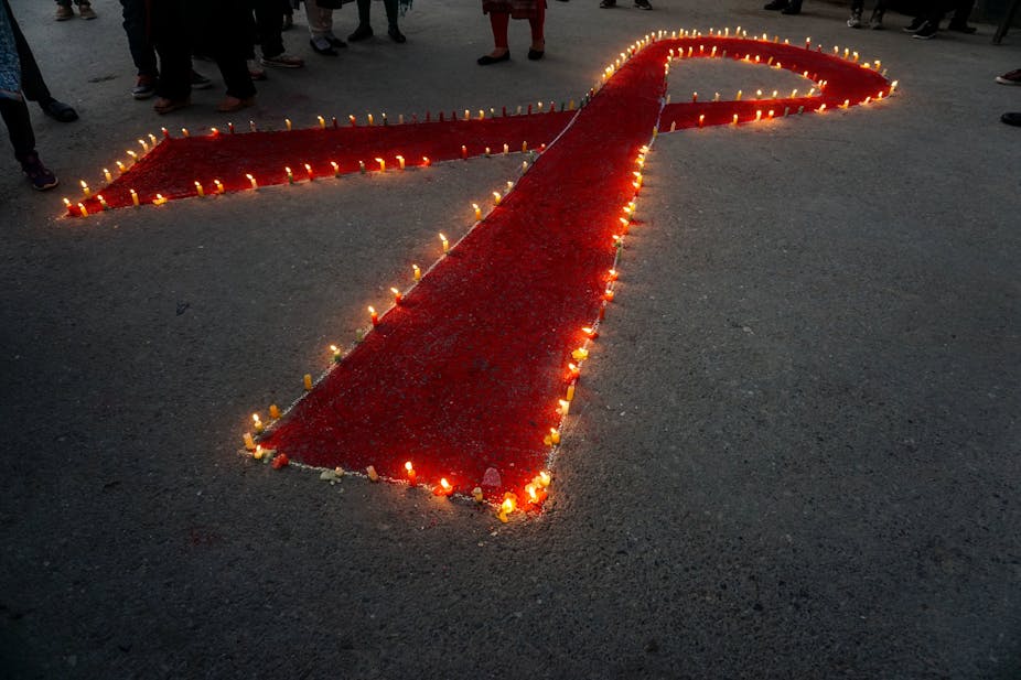 Women and children stand next to the candles lighting in a form of a Red Ribbon symbol. 