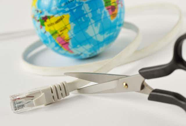 Scissors cutting an internet cable wrapped around a mini world