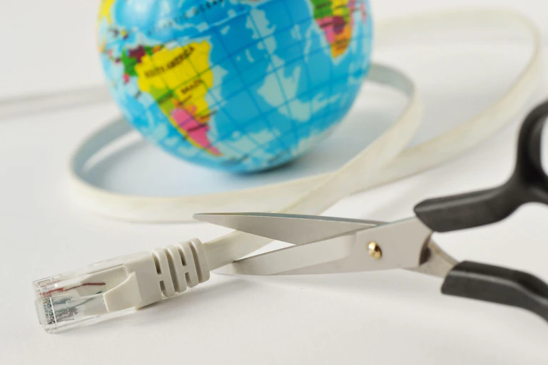 Scissors cutting an internet cable wrapped around a mini world