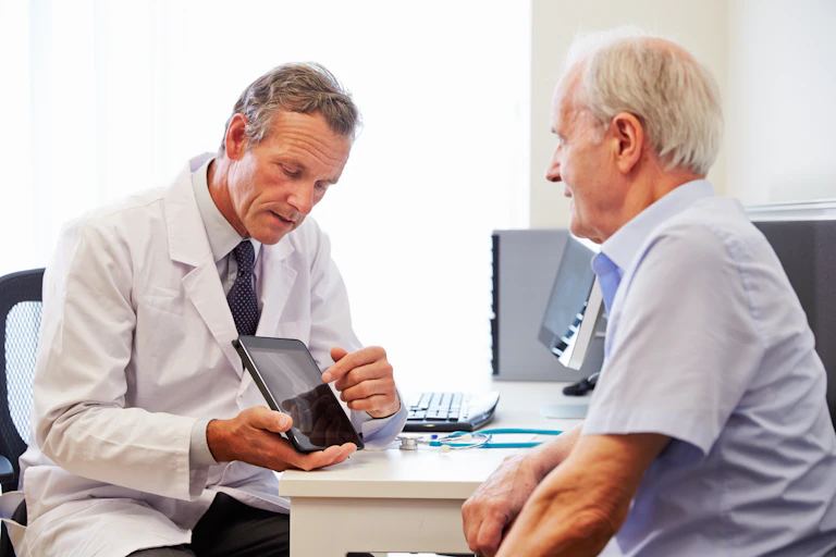 Doctor uses an iPad to explain an elderly man's diagnosis.